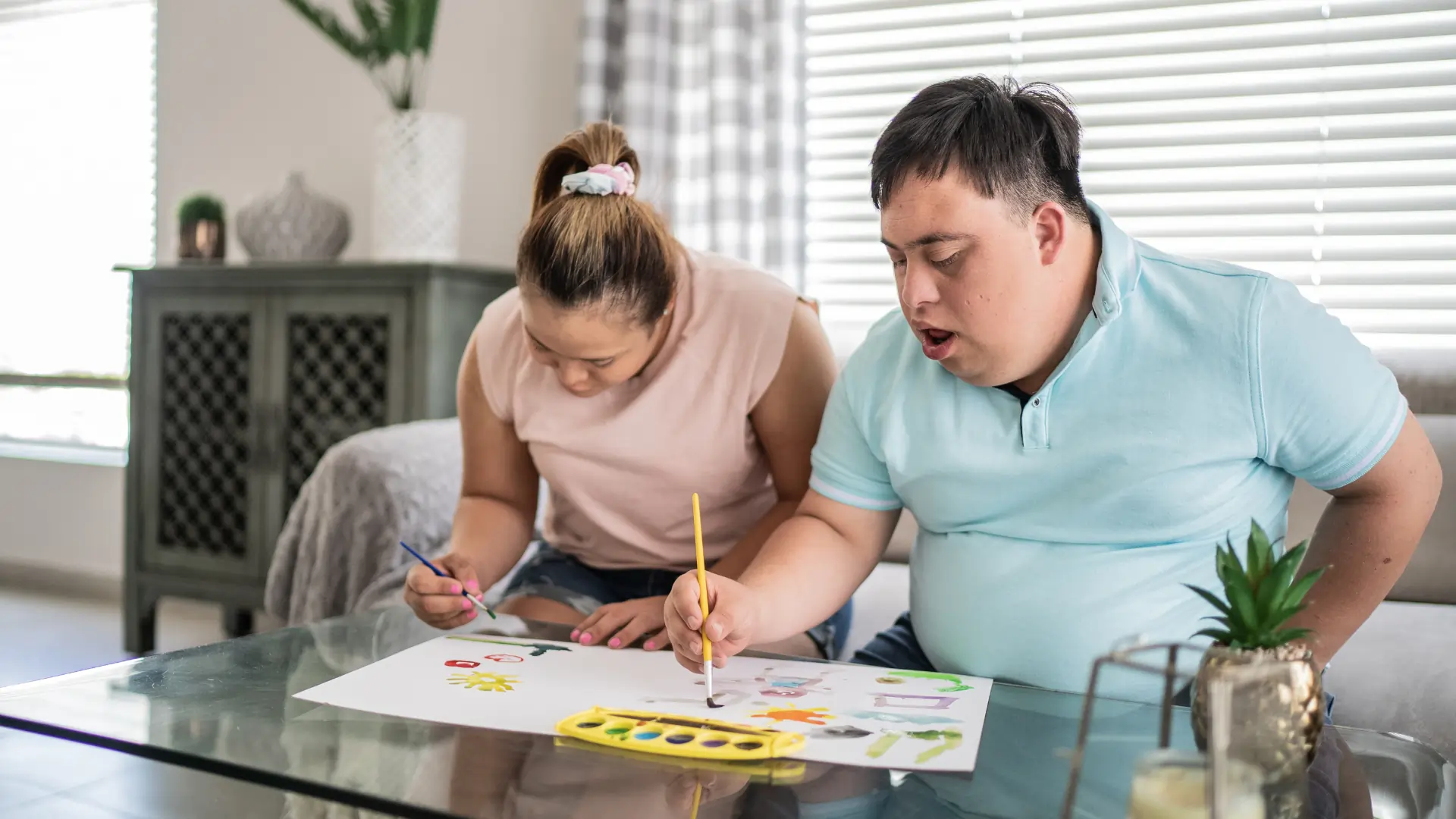 Young woman and young man with learning disability painting together at home.
